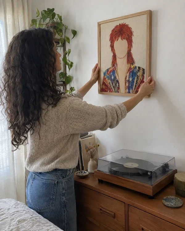 A woman hanging a framed portrait above a record player